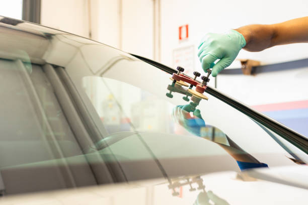 Mechanic with green gloves, in a garage replaces the broken windshield of a car with the help of tools. High quality photo