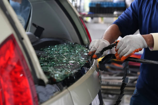 The cropped image shows an automobile glazier worker replacing the windscreen or windshield of a car at an auto service station garage, which was damaged by a car thief.