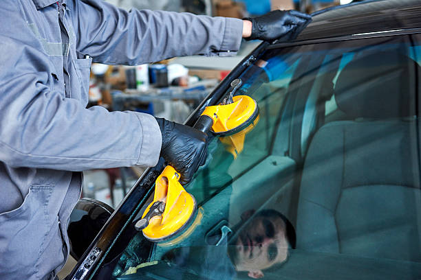 Glazier repairman mechanic worker replaces windshield or windscreen on a car in automobile workshop garage