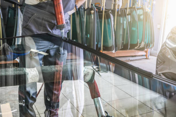 Process of preparing windshield for replacement in car service. Worker applies special adhesive sealant to windscreen before installation on auto.