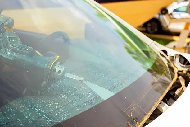 Technician using tool to remove damaged windshield from car.
