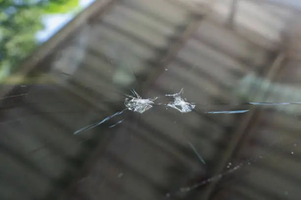 A close-up of a car windshield with visible cracks and small impact points.